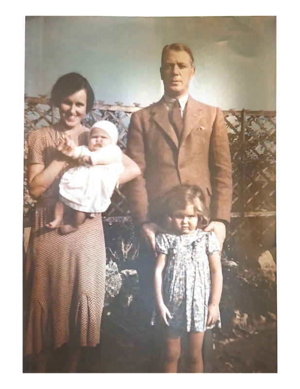 Scan of a color photograph of the Birch family when Jackie and Gill were young, approximately 1937. Anne is holding baby Gill and John is standing behind Jackie with his hands on her shoulders. 