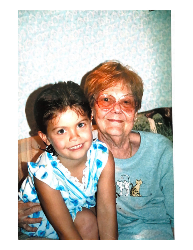 Scan of a color photograph of Jackie Turpin and Madison Cissell. Madison is sitting Jackie's lap on a couch in the living room. Madison is in her pajamas after a bath. Jackie is wearing a gray long-sleeve shirt with cats embroidered on it. 