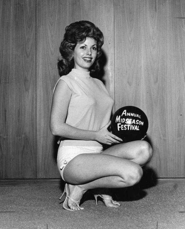 black and white photo of an beauty contestant smiling and posing for a promotional photo. She is kneeling down and holding a bowling ball with "Annual Midseason Festival" printed on it.