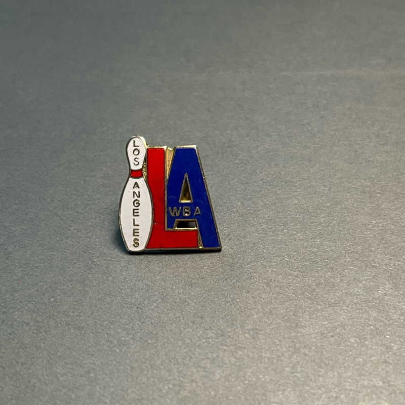 image of a lapel pin with an enamel and metal design of a white bowling pin and the letters "L" and "A" in red and blue enamel respectively. "Los Angeles WBA" are inlaid with gold metal.