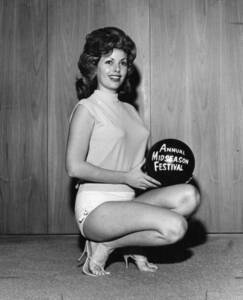 black and white photo of an beauty contestant smiling and posing for a promotional photo. She is kneeling down and holding a bowling ball with "Annual Midseason Festival" printed on it.