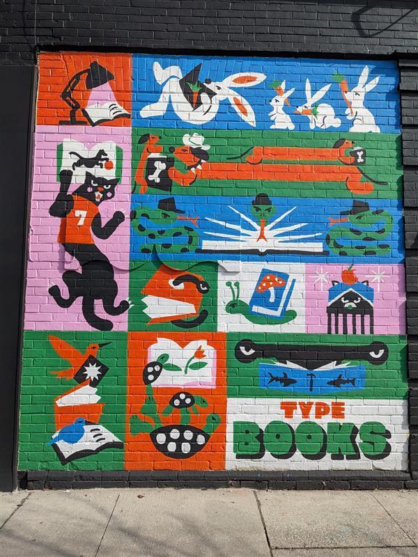 A mural on the side of a book store. The bottom of the image reads "Type Books" and there are colourful squares and rectangles featuring animals reading. Some examples include birds, turtles, and a snail.