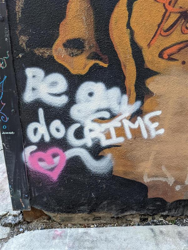 A tag on the side of a building in Graffiti Alley. The text reads 'be gay do CRIME'