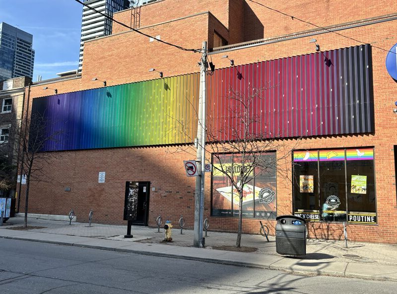 A metal, accordian-like rainbow painted strcuture on the side of a buidling