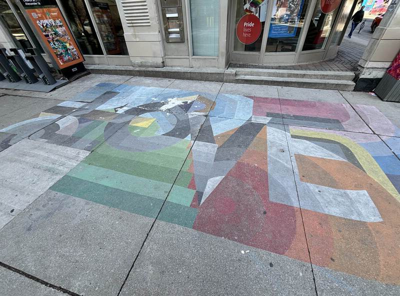 A multicoloured painted sidewalk featuring the word 'LOVE" in an abstract block-like design