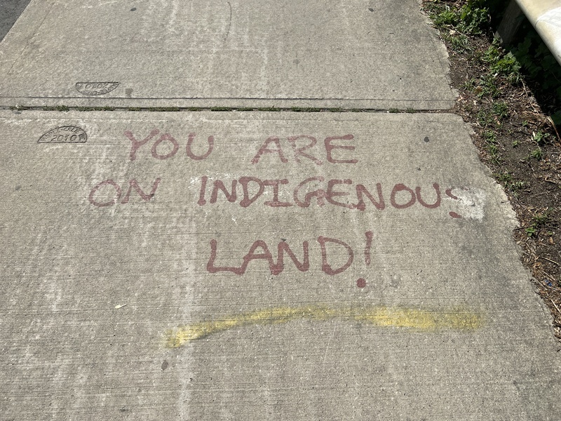 Text spray painted on the sidewalk saying "You are on Indigenous Land!"