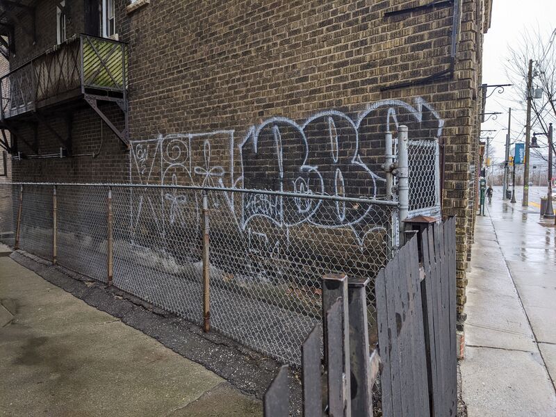 Side of a brick building with tags behinda chain fence.