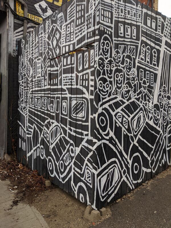 White mural on a black fence outside of a business depicting a city street.