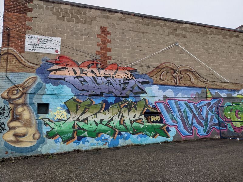 A bunny and brightly coloured graffiti across a brick wall.