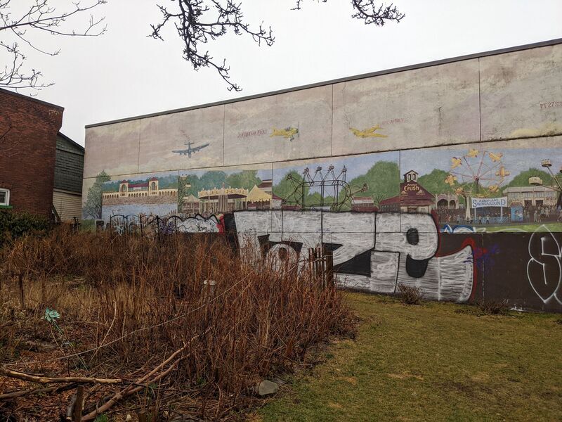 Mural of a carnival that is partially covered by large white letters and various tags.