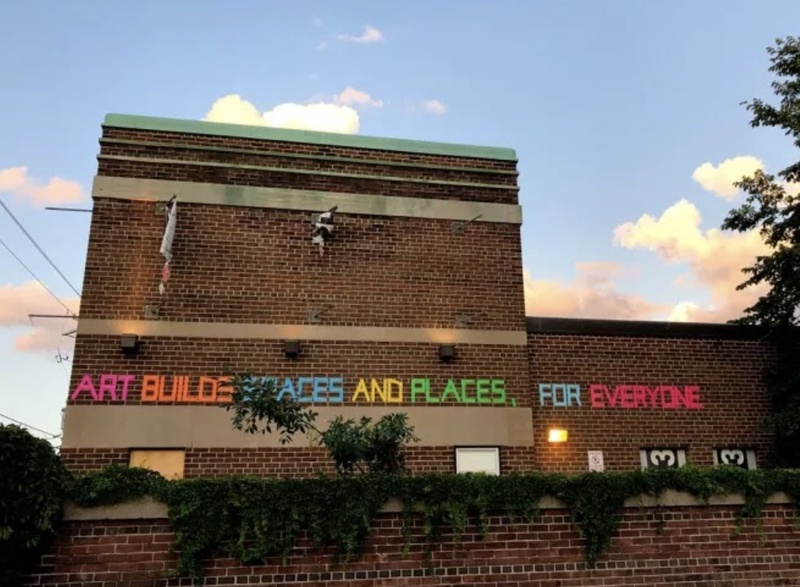 "Art Builds Spaces and Placed For Everyone" in bright rainbow colours on the side of a brick building.