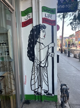 A woman with long hair wearing converse shoes holding the Iranian flag with the words "Woman Life Freedom" painted in the flag