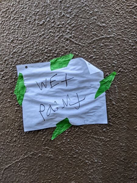 A wet paint sign on white paper attached with green tape to a wall.